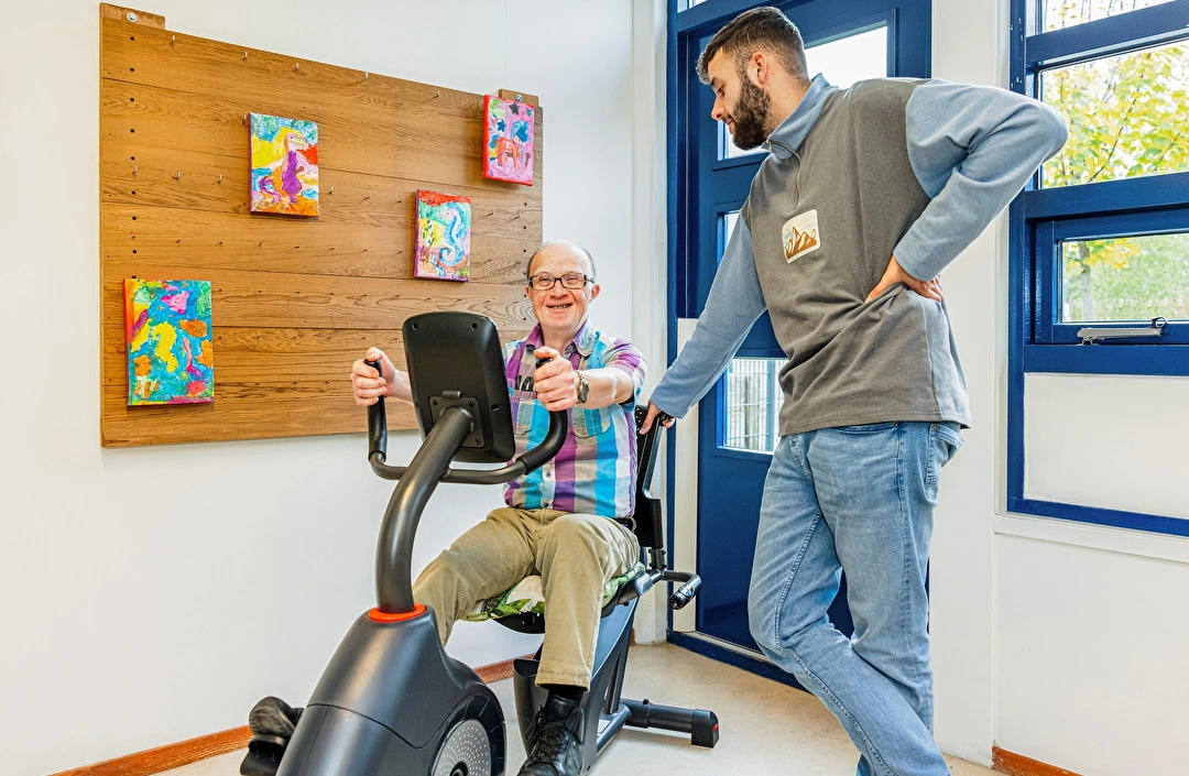 Geestelijk gehandicapte man op fitnessapparaat met verzorger