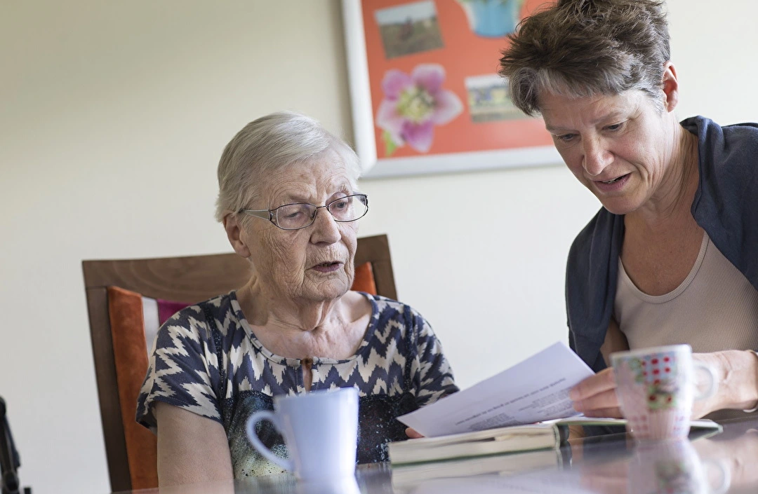 Oudere dame aan tafel leest samen met jongere dame een brief