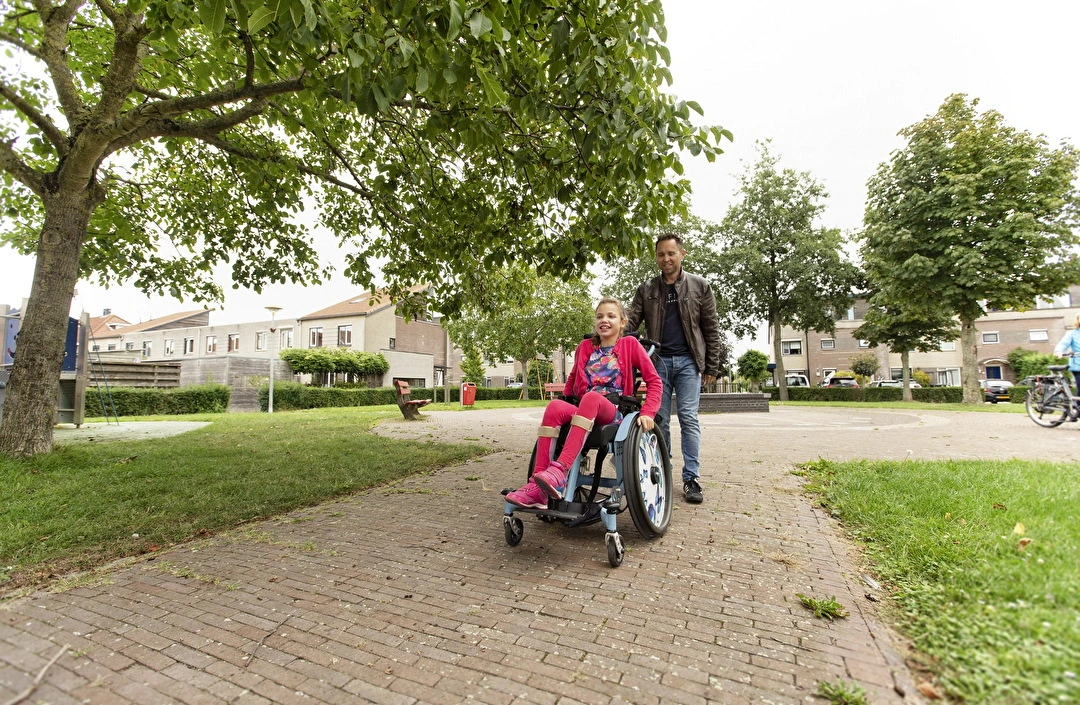 Vader wandelt door park met gehandicapte dochter in rolstoel 