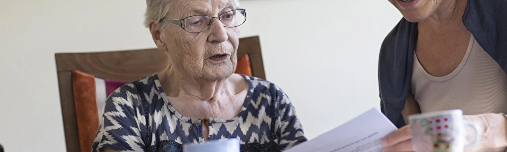 Oudere dame aan tafel leest samen met jongere dame een brief